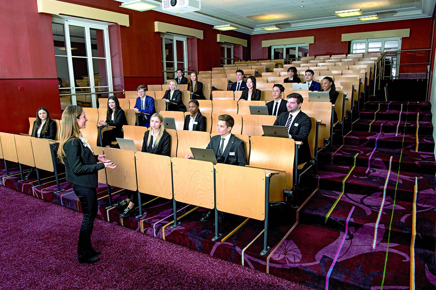 Students in business dress with laptops in the tiered BHMS lecture theatre